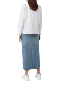 White long-sleeve blouse and a knee-length denim skirt. Sneakers are white. Skirt features back pockets and a subtle faded wash texture.