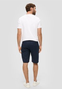 Marineblauwe pinstriped shorts van lichtgewicht stof, gecombineerd met een witte crew neck t-shirt, gedragen met witte sneakers. Ontspannen pasvorm, boven de knie.