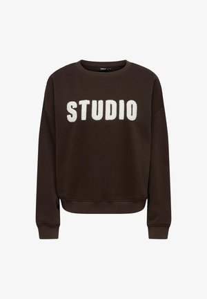 Sweatshirt brun avec un col rond et des poignets côtelés, affichant de grandes lettres blanches en peluche écrivant "STUDIO" sur le devant.