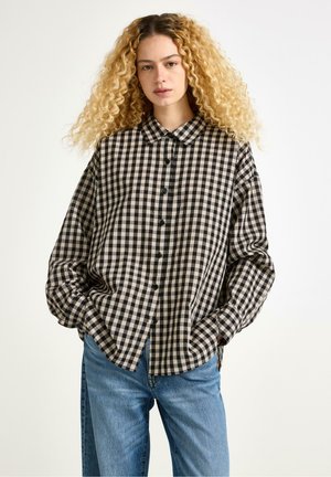 Camicia a quadri bianca e nera con colletto e spalle scese, abbinata a jeans in denim blu chiaro.