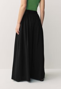 Svart, vida byxor med resårlinning, gjorda av ett texturerat tyg. Plagget flödar ner till strax ovanför anklarna.