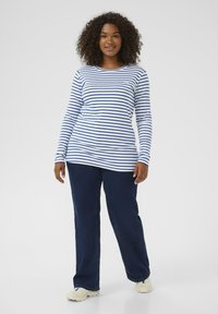 Long-sleeve striped shirt in white and blue, paired with dark blue jeans. The shirt features a crew neckline and fitted sleeves.