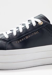 Baskets en cuir bleu marine avec des lacets blancs, détail de logo doré et une semelle plateforme blanche texturée avec des rayures diagonales.