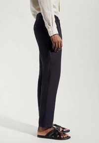 Räätälöidyt tummansiniset housut, joissa on slim fit ja sivutasku sekä ommeltu yksityiskohtia. Yhdistetty mustiin kudottuihin sandaaleihin.