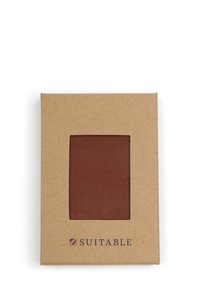 Bruine stofmonster in een kartonnen verpakking met een doorzichtig venster, met de merknaam "SUITABLE" gedrukt aan de onderkant.