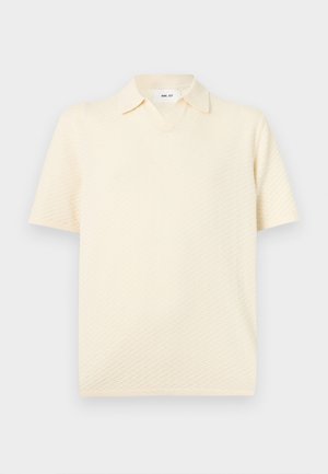 Κρεμ κοντομάνικο πικέ πόλο πουκάμισο με ανοιχτό γιακά και άνετη εφαρμογή, παρουσιάζεται σε απλό ανοιχτό φόντο.