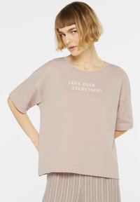 Helles rosafarbenes T-Shirt mit kurzen Ärmeln, rundem Ausschnitt und weißem Text "LOVE OVER EVERYTHING" auf der Vorderseite. Lässige Passform, weiche Textur.