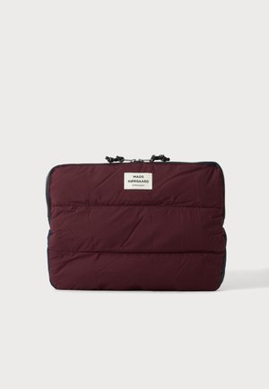 Vinrød polstret laptop-ærme med sorte lynlås træk og en hvid Mads Nørgaard Copenhagen label på en ensfarvet baggrund.