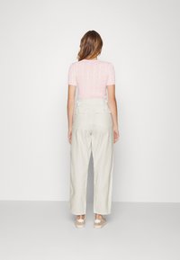 Rosa stickad topp med korta ärmar och flätmönster; högmidjade, vida krämfärgade byxor med knäppta bakfickor. Skor i neutrala toner.