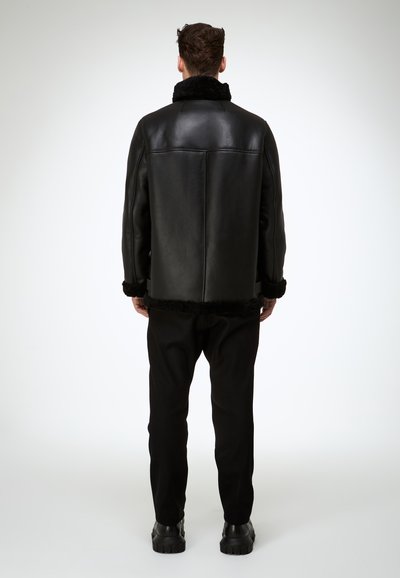 Schwarze Lederjacke mit Pelzkragen und Saum, mit kastiger Form und glatter Textur. Kombiniert mit schwarzer Hose und klobigen Stiefeln.