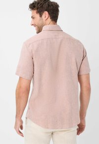 Camicetta a maniche corte in tessuto texturizzato di un delicato rosa, con colletto classico, orlo curvo e dettagli di cucitura sottili.