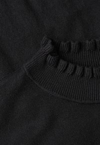 Gros plan d'un pull en maille noire montrant un col montant côtelé et une texture tricotée détaillée.