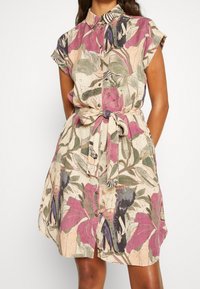 Abito camicia a maniche corte in tessuto leggero, caratterizzato da un motivo floreale con accenti rosa e verdi, colletto e vita cinturata.