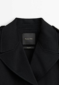 Czarny wełniany płaszcz z szerokim klapami i zbudowanymi ramionami. Posiada metkę z logo wewnątrz, prezentującą czyste linie i dopasowany krój.