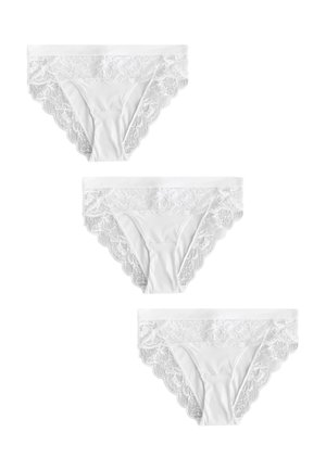 Kobieta ubrana w biały biustonosz z koronkowym wykończeniem i pasujące majtki ozdobione koronką na jednolitym tle.