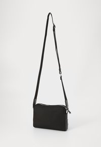 Black crossbody bag made of canvas with a smooth texture, featuring a zipper closure and an adjustable strap. Minimalist rectangular design.