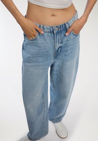 Jasnoniebieskie, wysokie dżinsy oversize z kieszeniami z przodu i suwakiem. Tkanina ma miękką teksturę i subtelne wyblaknięcia.