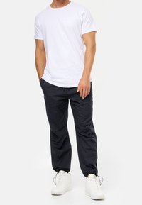 Witte crewneck t-shirt gecombineerd met zwarte joggerbroek met trekkoord en witte sneakers. De broek heeft een verfijnde pasvorm en elastische boorden.