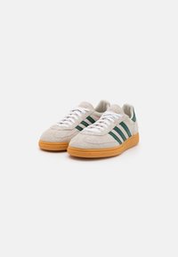Beige suede sneakers with green stripes, white laces, and orange rubber outsole. Rounded toe and textured upper for added grip.