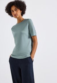 Světle zelený top s krátkým rukávem vyrobený z hladké látky, v kombinaci s námořnicky modrými širokými kalhotami s plisováním a kapsami. Jednoduchý, klasický design.