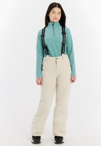 Beige geïsoleerde sneeuwbroeken met bretels, gecombineerd met een lichtblauwe fleece top met rits. De stof is glad en geschikt voor winterse activiteiten.