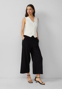 White, striped, sleeveless vest with a V-neck and buttons, paired with loose, black wide-leg trousers and black heeled sandals.