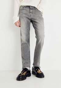 Lys grå denimjeans med rett ben og subtile slitasjer. Brukt med svarte sko med teksturert design og kraftig såle.