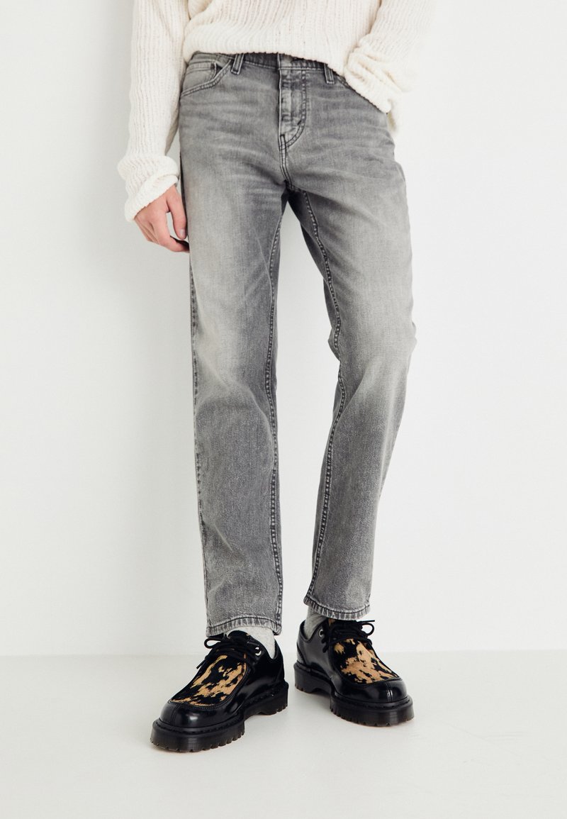 Lys grå denimjeans med rett ben og subtile slitasjer. Brukt med svarte sko med teksturert design og kraftig såle.