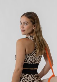 Sportski top s uzorkom leoparda koji ima prilagođeni kroj, naramenice i kontrastni crni pojas. Teksturirana tkanina s vidljivim šavovima.