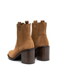 Brązowe zamszowe botki za kostkę z zaokrąglonym noskiem, elastycznymi panelami bocznymi i masywnym, drewnianym obcasem, charakteryzujące się gładką fakturą i minimalnymi detalami.