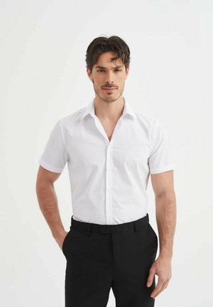 Chemise blanche à manches courtes avec un col, associée à un pantalon noir. Texture lisse, coupe standard et design classique.