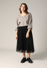 Pull-over gris à col en V côtelé avec des manches bouffantes, associé à une jupe midi en tulle plissé noire et des chaussures compensées noires à lacets.