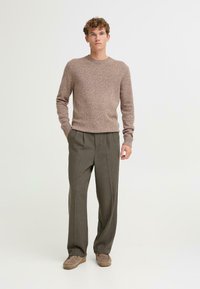 Gebreide trui in lichtbeige met subtiele textuur, gecombineerd met lichtgrijze broeken met plooien, gedragen met tan suede schoenen.