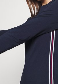 Marinblus med lång ärm som har en kontrasterande vertikal rand i rött och vitt längs sid sömmen. Mjuk tygtextur.