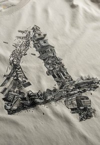 Beige t-shirt met een zwart grafisch ontwerp dat een collage van gebouwen en machines toont, die samen de vorm van de letter "L" vormen.
