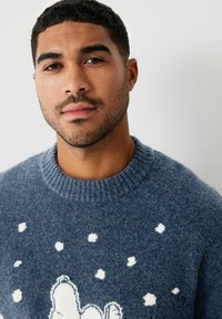 Maglione lavorato a maglia blu scuro in morbida lana, con una grafica di un orso bianco e motivi di fiocchi di neve sulla parte anteriore. Collo rotondo a coste.