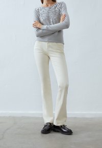 Maglione grigio a maniche lunghe con paillettes argento sulle spalle, abbinato a pantaloni color crema e scarpe nere chunky. Texture liscia, design aderente.