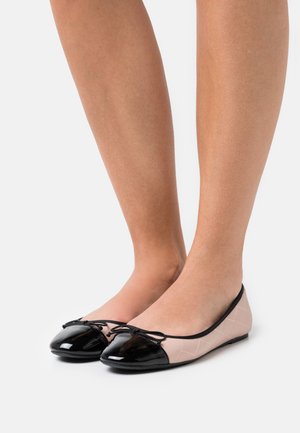 Ballerines avec une texture matelassée nude, un capuchon noir brillant et un détail en nœud. Matériau doux, forme arrondie et design minimaliste.