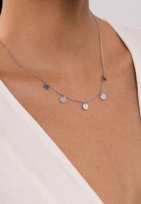 Silberne Halskette mit einer zarten Kette, die fünf kleine, polierte, runde Anhänger in unterschiedlichen Positionen zeigt und eng am Hals getragen wird.