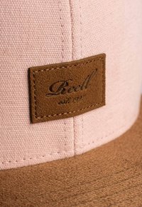 Cap features a pink woven fabric crown and a brown textured leather brim with a rectangular leather patch embossed with "Reell est. 1997."