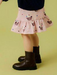 Bottines en cuir marron avec une semelle robuste, associées à une jupe rose ornée d'un motif de cupcakes et d'accents en forme de cœur.