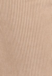 Beige ribbelstof close-up, met een zachte textuur en verticale lijnen. Het materiaal lijkt rekbaar met subtiele variatie in toon.