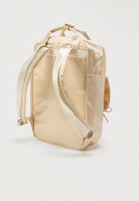 Μπεζ σακίδιο νάιλον με ρυθμιζόμενους ιμάντες, επάνω λαβές, πλευρική τσέπη και απαλή υφή. Διαθέτει μεταλλικά αξεσουάρ.