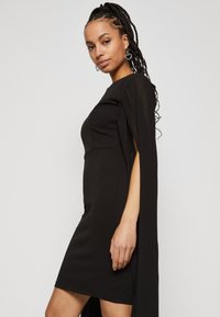 Μαύρο φόρεμα με εφαρμοστό κορσέ και ρο-flow μανίκια. Φτιαγμένο από υφασμάτινη υφή, μέχρι το γόνατο με πλαϊνές σχισμές για επιπλέον λεπτομέρεια.