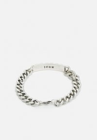 Pulseira de corrente de prata com uma etiqueta plana exibindo "ICON." Apresenta elos entrelaçados, uma textura suave e um acabamento polido.