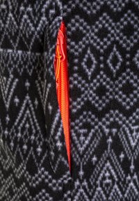 Fleece nero e grigio con un design geometrico; presenta una cerniera arancione sul lato per una chiusura sicura.