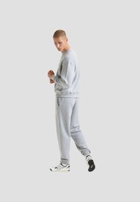 Felpa grigia e pantaloni sportivi realizzati in tessuto morbido, con una vestibilità comoda. Dettagli notevoli includono polsini e vita a costine e cuciture a contrasto.