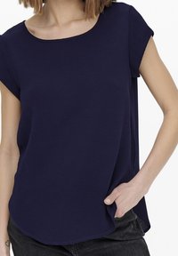 Top blu navy a maniche corte con scollatura rotonda, vestibilità comoda e tessuto strutturato. Orlo curvo con spacchi laterali per facilitare i movimenti.