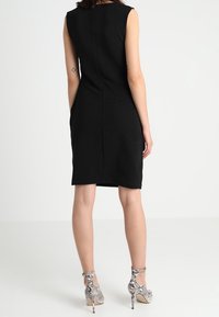 Schwarz ärmelloses Kleid mit figurbetonter Silhouette, strukturiertem Stoff und Rückennahtdetails, kombiniert mit silbernen High-Heels im Schlangenhautmuster.
