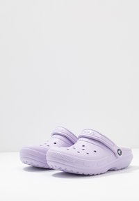 Zoccoli in gomma viola con perforazioni, una cinghia posteriore e una suola testurizzata. Il design è leggero e facile da pulire.